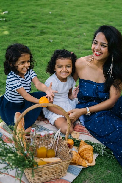 A woman in a blue dress enjoys a picnic with two girls on a sunny afternoon