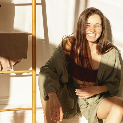 Giovane donna sorridente in una stanza e illuminata dalla luce del sole: "È nella semplicità che risiede la vera ricchezza..."