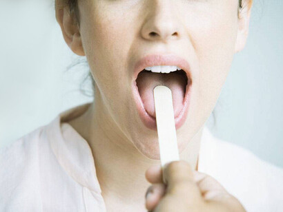 A physician examining a woman's throat with a tongue depressor to explore the cause of sore throat and to rule out acid reflux