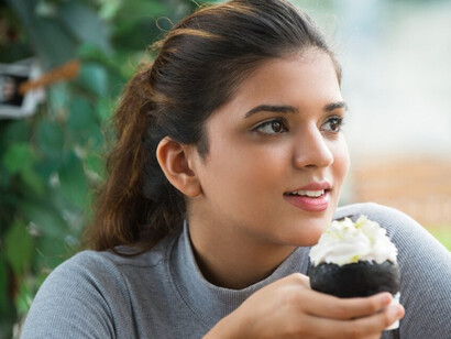 A young Indian woman enjoying a creamy pastry in a café, highlighting the rising trend of sugar consumption in India