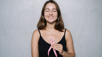 A woman wearing a black spaghetti strap top holds a pink ribbon, symbolizing breast cancer awareness