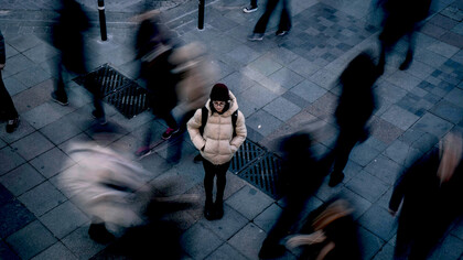 A woman stands alone in a busy crowd as people pass by, symbolizing loneliness