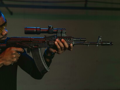 Em posição de disparo, atirador pratica manejo de fuzil AKM. A imagem remete ao ambiente de tensão e violência política relatado no texto
