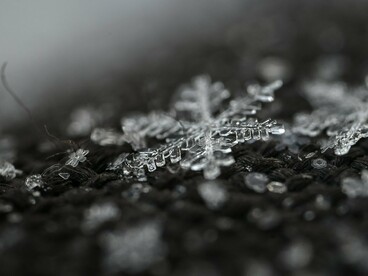 Highlighted against a dark, out-of-focus backdrop, a symmetrical snowflake reveals its delicate branches and hexagonal center, a quintessential symbol of winter's touch
