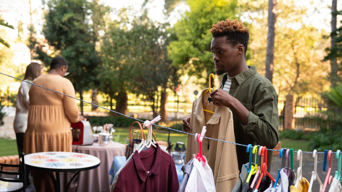 A man sifts through second-hand clothes at a yard sale, making mindful choices to resist the lure of fast fashion and support a more sustainable, circular economy