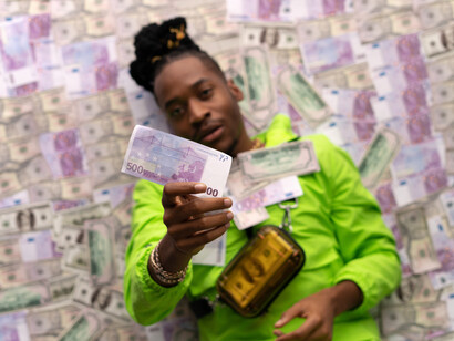 A man, laying on a bed of money, holds up more money