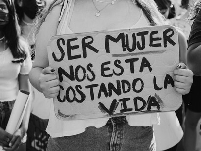 Manifestante exibe o cartaz "Ser mujer nos está costando la vida" durante ato público. O combate às discriminações de gênero integra uma das dimensões centrais da resistência defendida no artigo