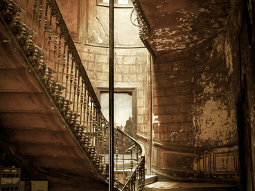 A dark, decaying interior where cracked and broken tiles lie unevenly across the floor near the stairs