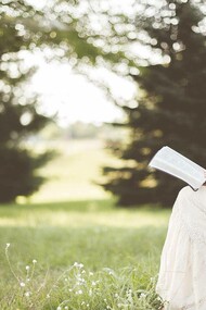 A blonde woman in a field reading a novel written by either Virginia Woolf 