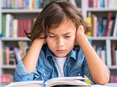 A child sitting at a desk, staring at schoolwork with visible frustration, representing the growing challenge of sustained attention in a distracted age