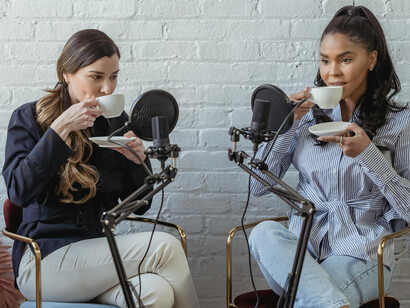 In a broadcasting studio, a diverse group of women share ideas and dialogue around their microphones