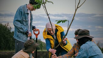 Groupe de bénévoles plantant un arbre sous les conseils de leur chef en gilet jaune