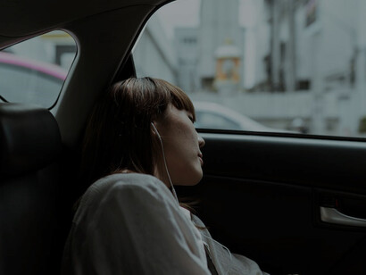 As the car moves away, a serene woman finds solace in the backseat, her earphones playing soothing music, her countenance touched by both tranquility and a hint of sorrow