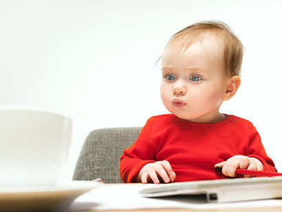 A joyful toddler girl eagerly explores a computer keyboard, demonstrating her natural curiosity and fascination with technology