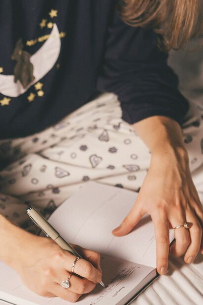 A young woman writing in her journal while sitting on her bed, captured in a quiet and intimate moment of reflection