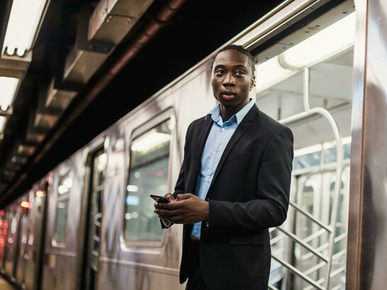 Confident young man in a suit using a smartphone while standing on a subway platform in a modern urban setting