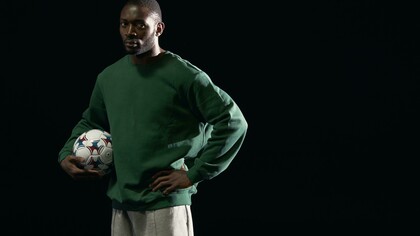 A man in a green sweater holding a soccer ball