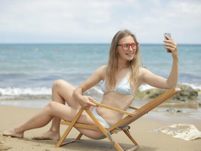 Garota se fotografa no celular enquanto relaxa na praia. Quase conseguimos saber tudo em tempo real, então nem selecionamos, nem interpretamos ou se quer digerimos cada acontecimento. Tudo passa por uma ordem de comunicação tão imediata que nos tornamos reféns do mundo