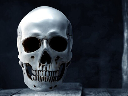 A human skull sits on a wooden table, illuminated by a dark, moody background