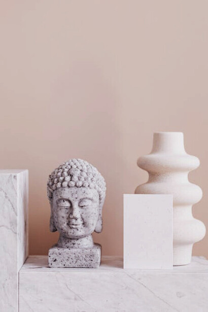 The stone bust of Buddha embodies the Buddhist teaching that true freedom from suffering comes from embracing both pleasure and pain, achieving a state of equanimity