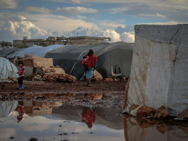 In Idlib, Idlib Governorate, Syria, a refugee camp unfolds across muddy ground, where rows of tents shelter people living in difficult conditions