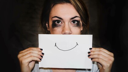 Communicating the false sense of happiness by drawing a smile on a piece of paper and hanging it in front of the mouth to mask the misery