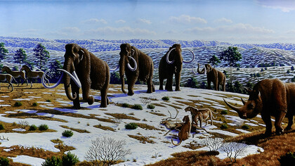 A group of prehistoric hunters confronts a gigantic mammoth in a lush, sunlit forest setting