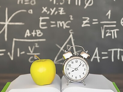 Book with apple and alarm clocks near blackboard