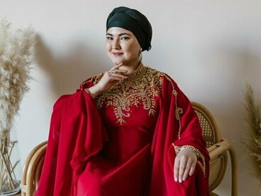 A woman dressed in an ornate red traditional gown with intricate gold embroidery and a black head covering, representing cultural heritage expressed through clothing