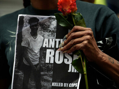 A woman holds a rose and a sign for Antwon Rose