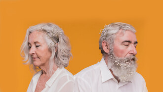 An elderly couple smiling warmly while posing with a bouquet of flowers