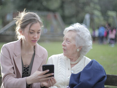 A daughter patiently teaching her elderly mother how to use a smartphone