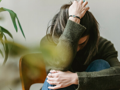 Woman sitting on a chair hugging her knees, overwhelmed by negative thoughts