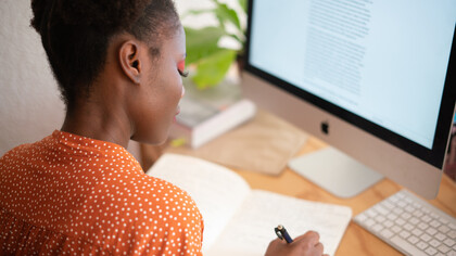 Mulher copia um texto do computador em seu caderno de anotações
