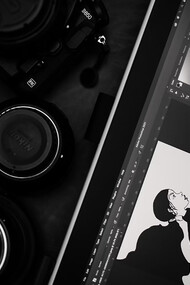 A black and silver DSLR camera placed beside a tablet, where someone is drawing—capturing a moment of creativity in action