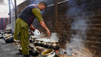 A man stirs food in large pots over an open flame, preparing a traditional meal, Srinagar, India