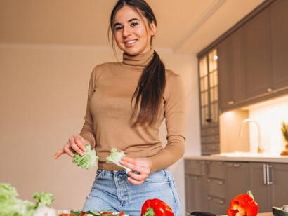 A woman cooking a nutritious plant-based meal in the kitchen, with a variety of fresh vegetables and fruits, highlighting vegan nutrition