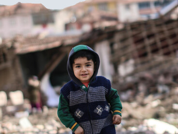 A young child standing before a city in ruins, Malatya, Türkiye
