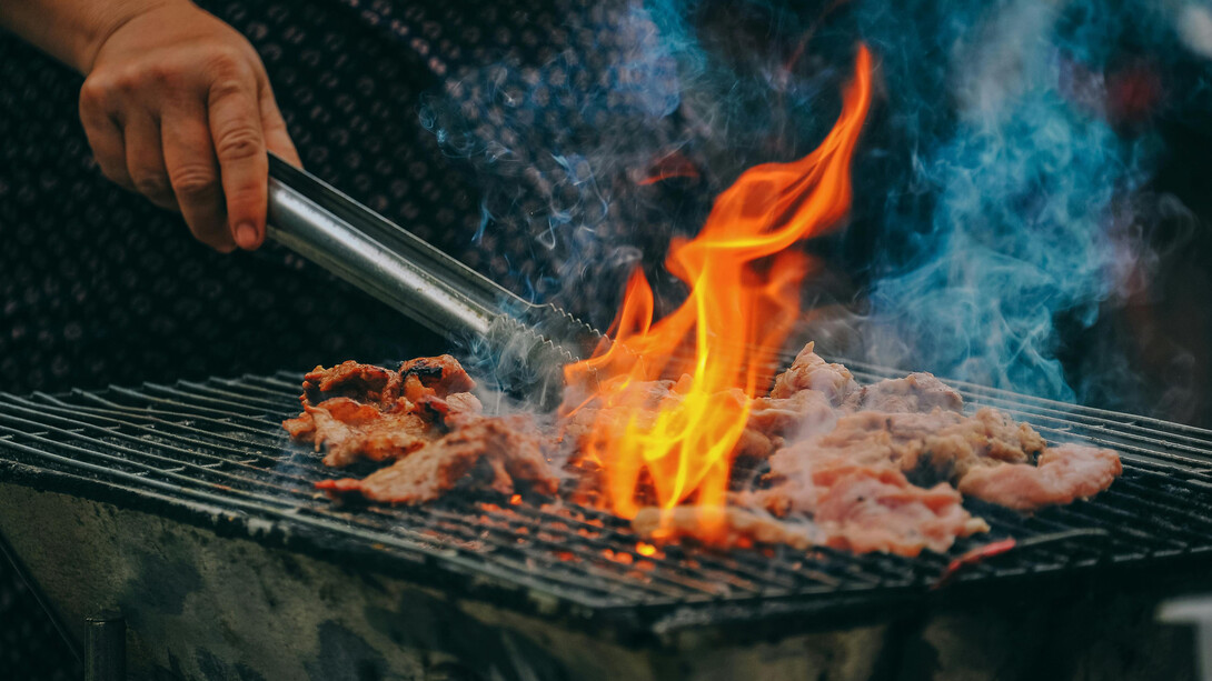 A close-up of a man grilling meat, with charcoal flames rising and adding a smoky touch to the cooking process