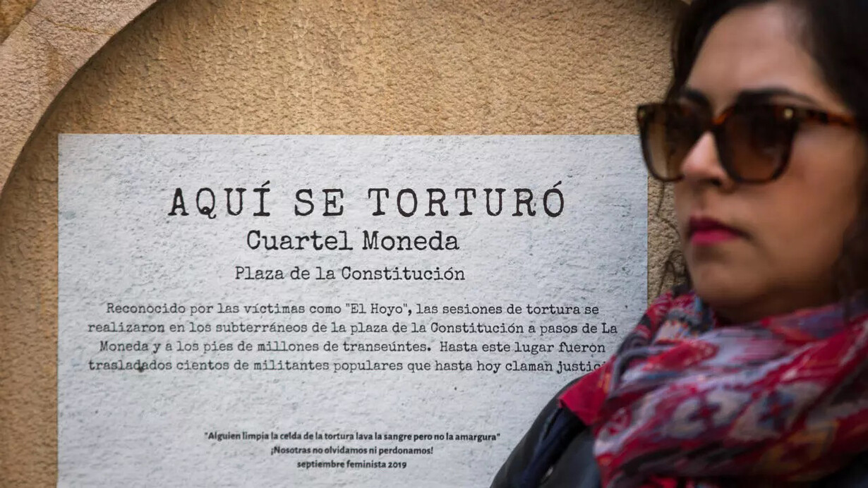 Una mujer se manifiesta frente a un cartel que conmemora uno de los centros de tortura de la dictadura de Augusto Pinochet en Santiago de Chile