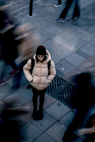 A woman stands alone in a busy crowd as people pass by, symbolizing loneliness