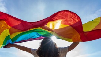  A young woman waving LGBTQIA+ flag under the sky