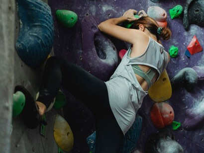 A woman climbing steadily up an indoor rock wall, representing the courage to move forward despite uncertainty