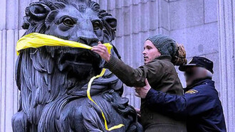 Una manifestante pone una mordaza a uno de los leones del Congreso de los Diputados en Madrid