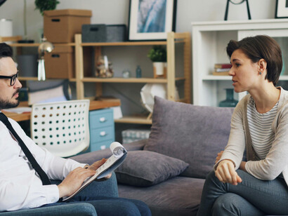 A man and a woman sitting on a couch as the woman engages in a therapy conversation