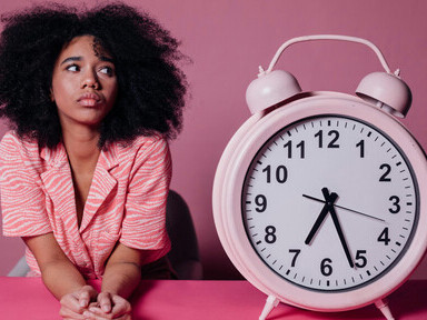 Woman looking thoughtfully at an oversized pink alarm clock, a concept of time