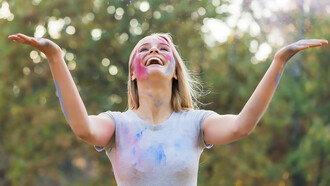 Happy woman enjoying a playful moment with powdered color, celebrating the joy of life and the connection between happiness and physical well-being