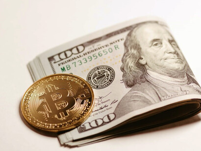 A stack of one hundred dollar bills and a bitcoin