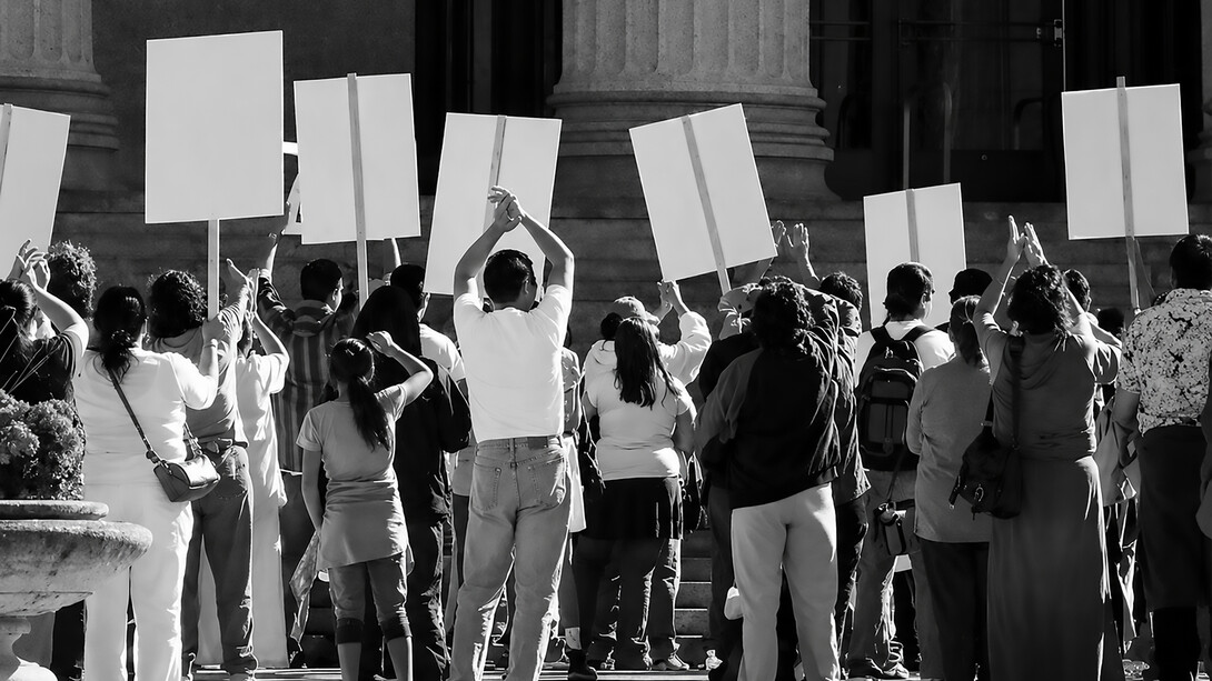 A crowd of protesters gathers at a political demonstration, holding signs and expressing their frustration