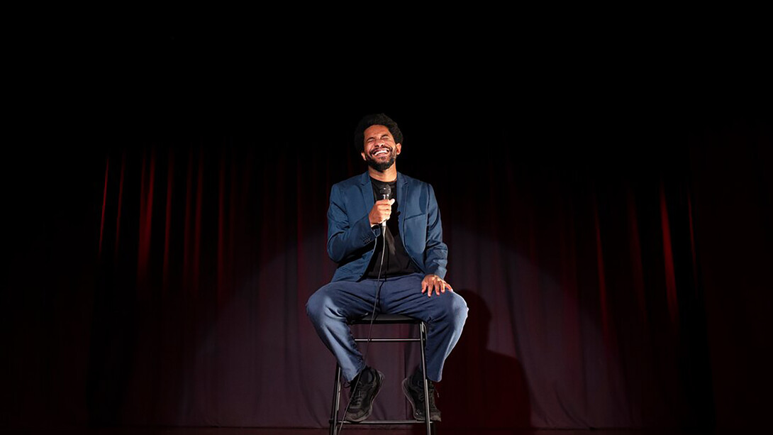 A man performing stand-up comedy on stage in a lively comedy club atmosphere